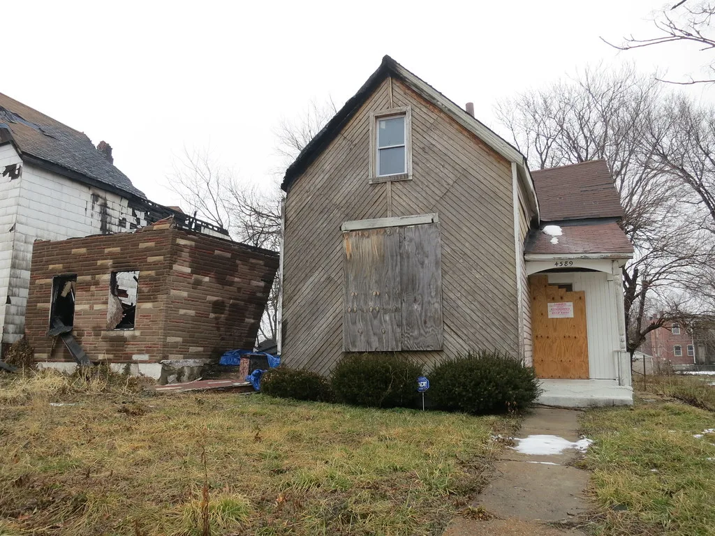 Petite maison aux ouvertures condamnées jouxtant une maison incendiée aux murs effondrés.