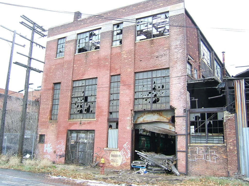 Usine de briques abandonnée aux grandes verrières cassées et à la porte métallique écrasée.