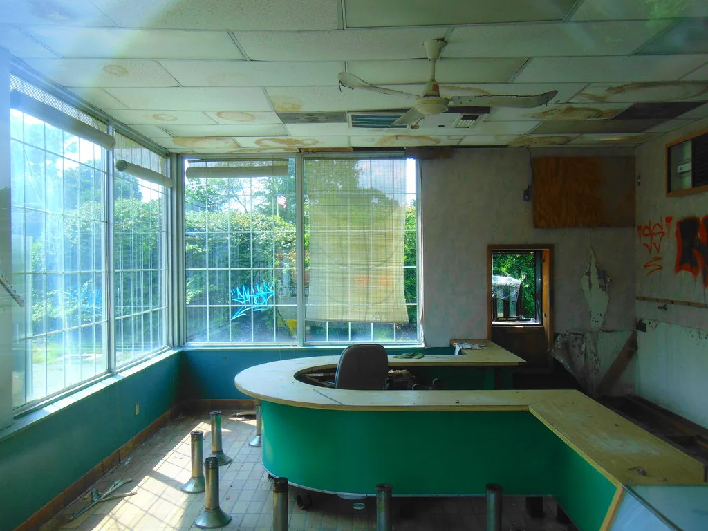 Green counter in a former establishment with dismantled seats, stained ceiling and peeling walls.