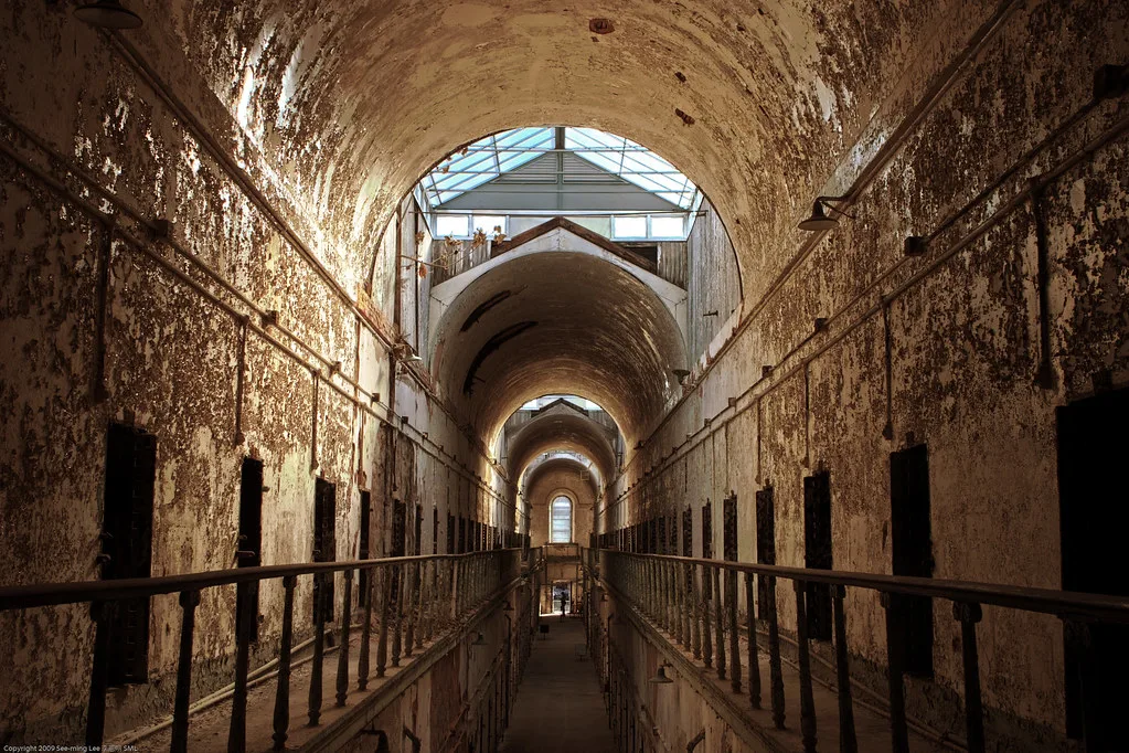 Galerie voûtée d’une ancienne prison avec cellules ouvertes et peinture écaillée.