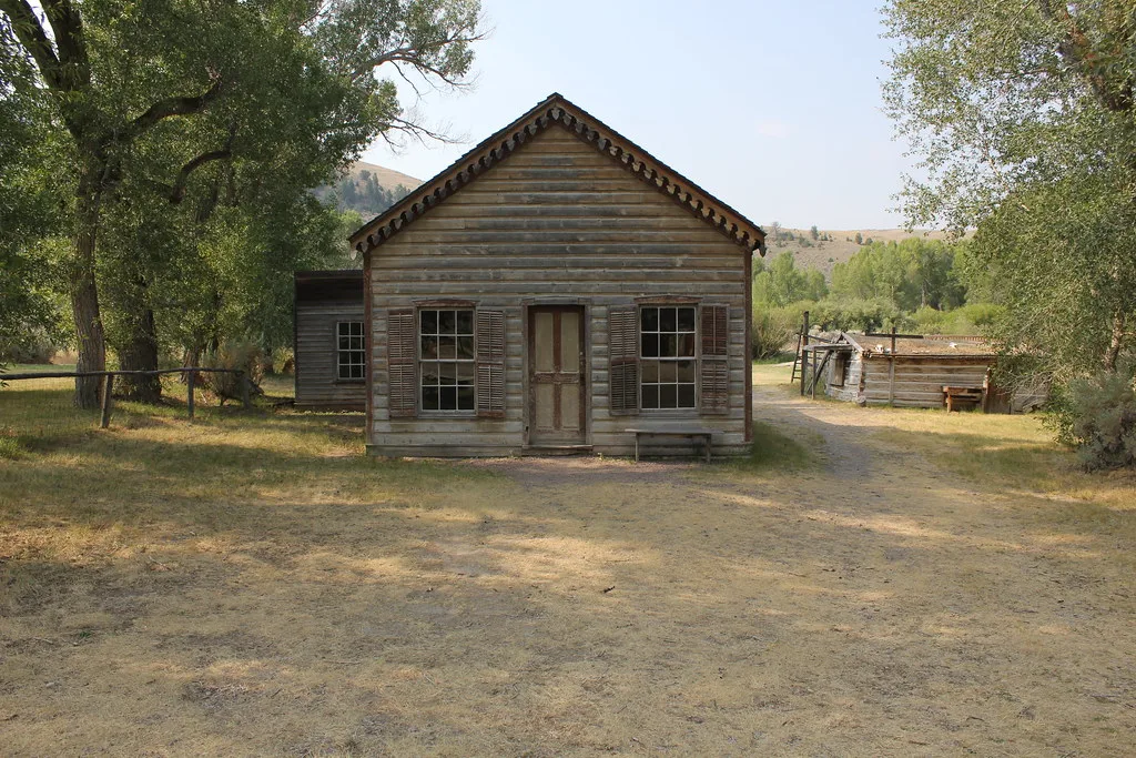 Old wooden house with open shutters beside a damaged outbuilding.