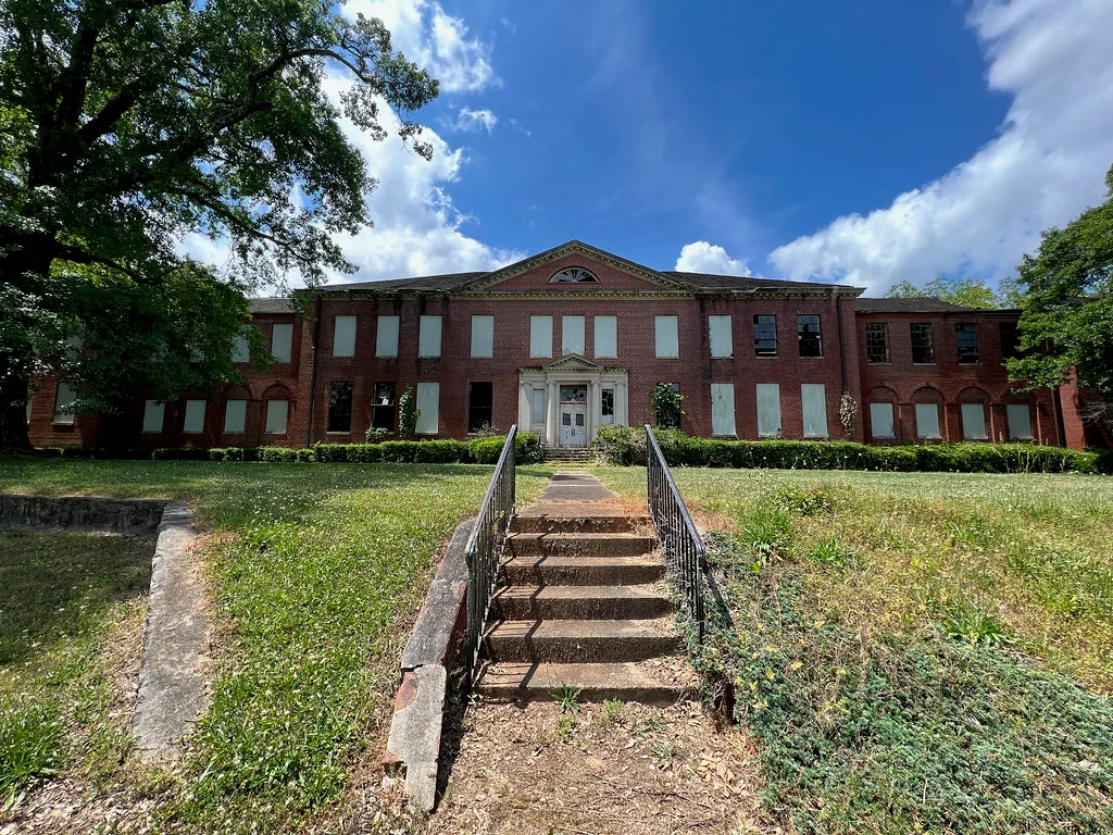 Large brick building with boarded windows above a flight of steps.