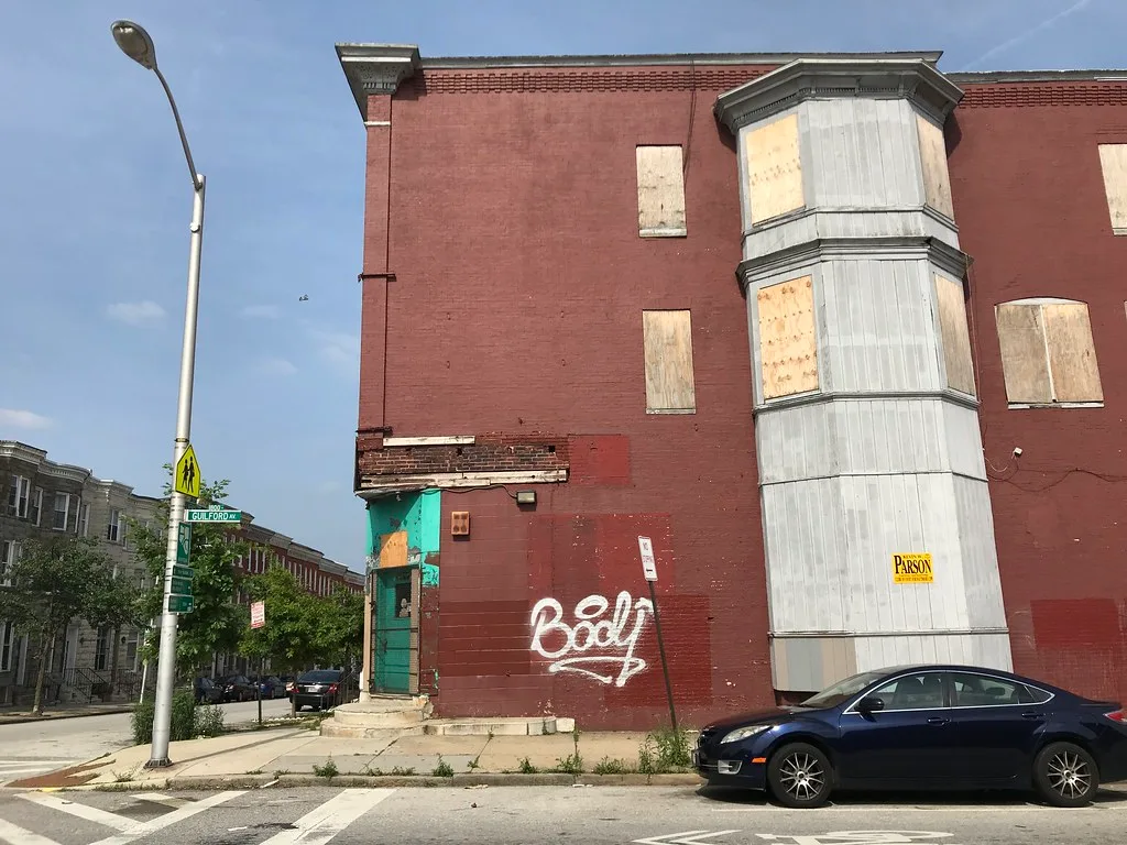 Old corner house with boarded windows and a graffiti-covered wall.