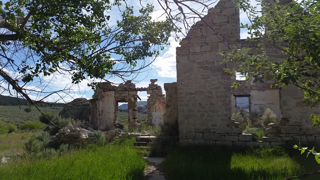 Ruins of a pale stone house without a roof, with broken walls and empty openings in tall grass.
