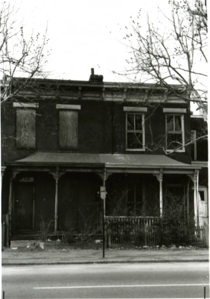 Old black-and-white photograph of a boarded-up house with a dilapidated porch.