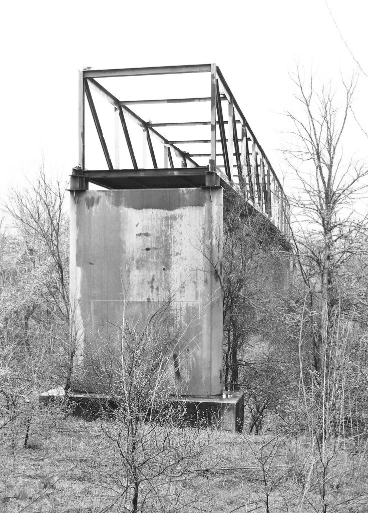 Span of a disused bridge ending on a tall concrete pier amid scrub.