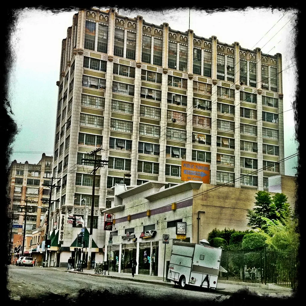 Large urban building with broken windows and boarded openings above street-level shops.