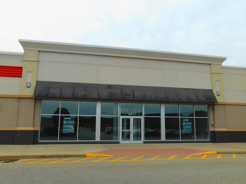Glazed frontage of a vacant store in Killingly beneath a dark canopy.