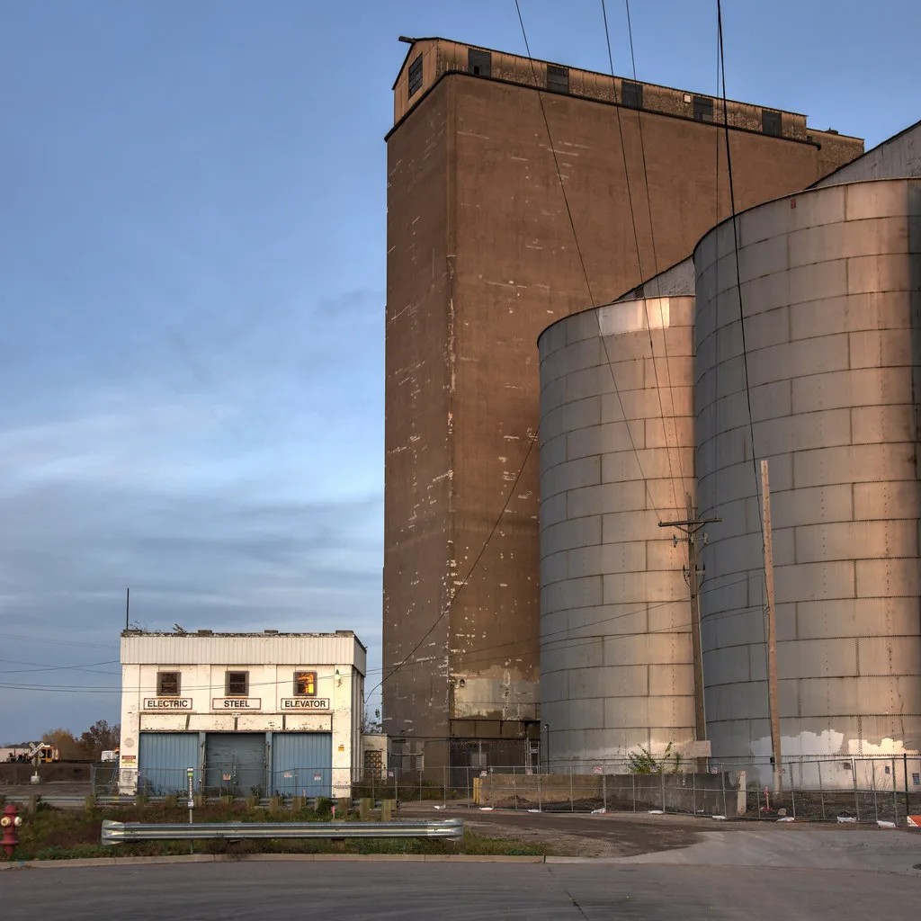 Old metal silos and a brown grain elevator behind fencing.
