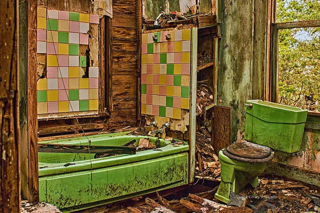 Salle de bains dégradée avec baignoire et toilettes vertes parmi les débris.