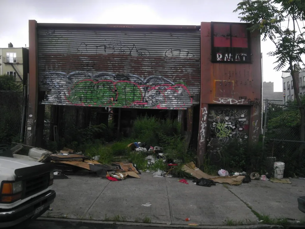 Ancienne devanture taguée envahie de végétation et de déchets.