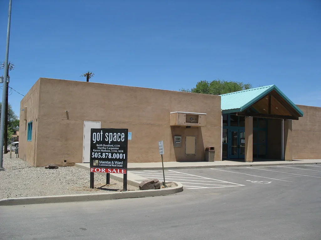 Vacant former bank with a beige facade and an entrance under a green canopy.