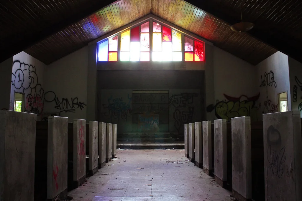 Interior of an abandoned chapel beneath coloured glazing.