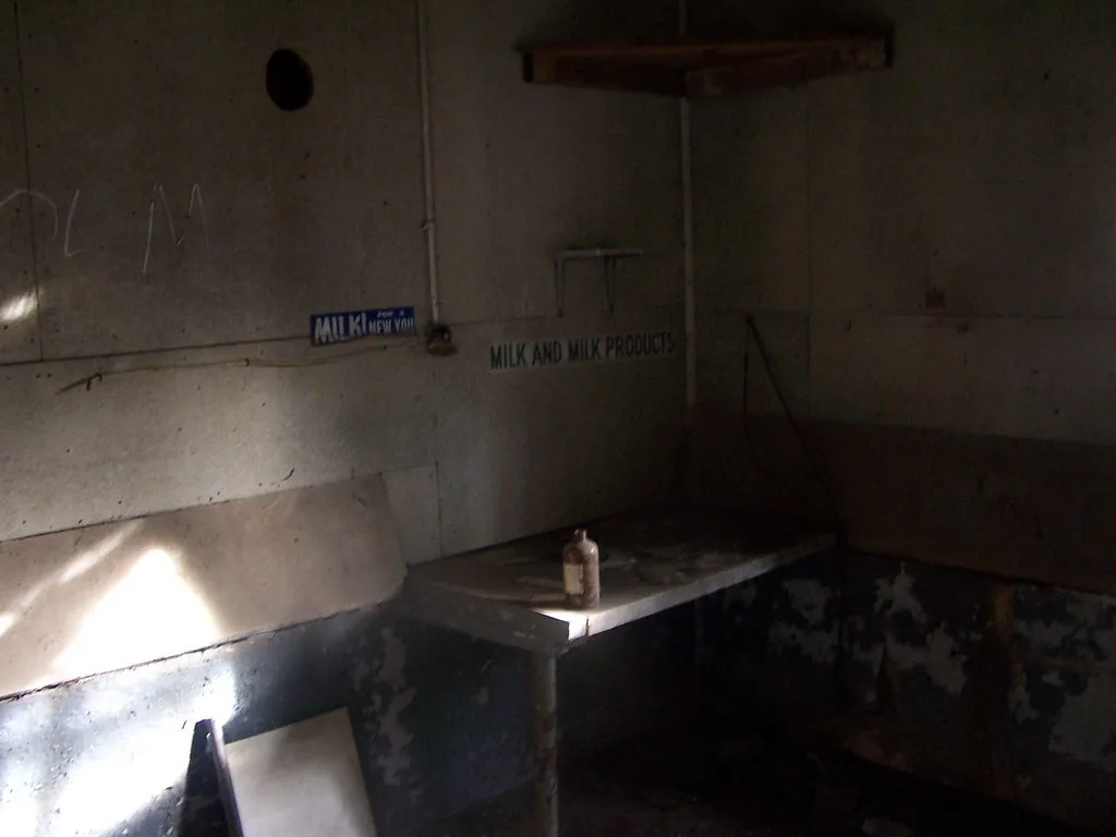 Petite pièce abandonnée aux murs écaillés avec une bouteille sur un ancien comptoir.