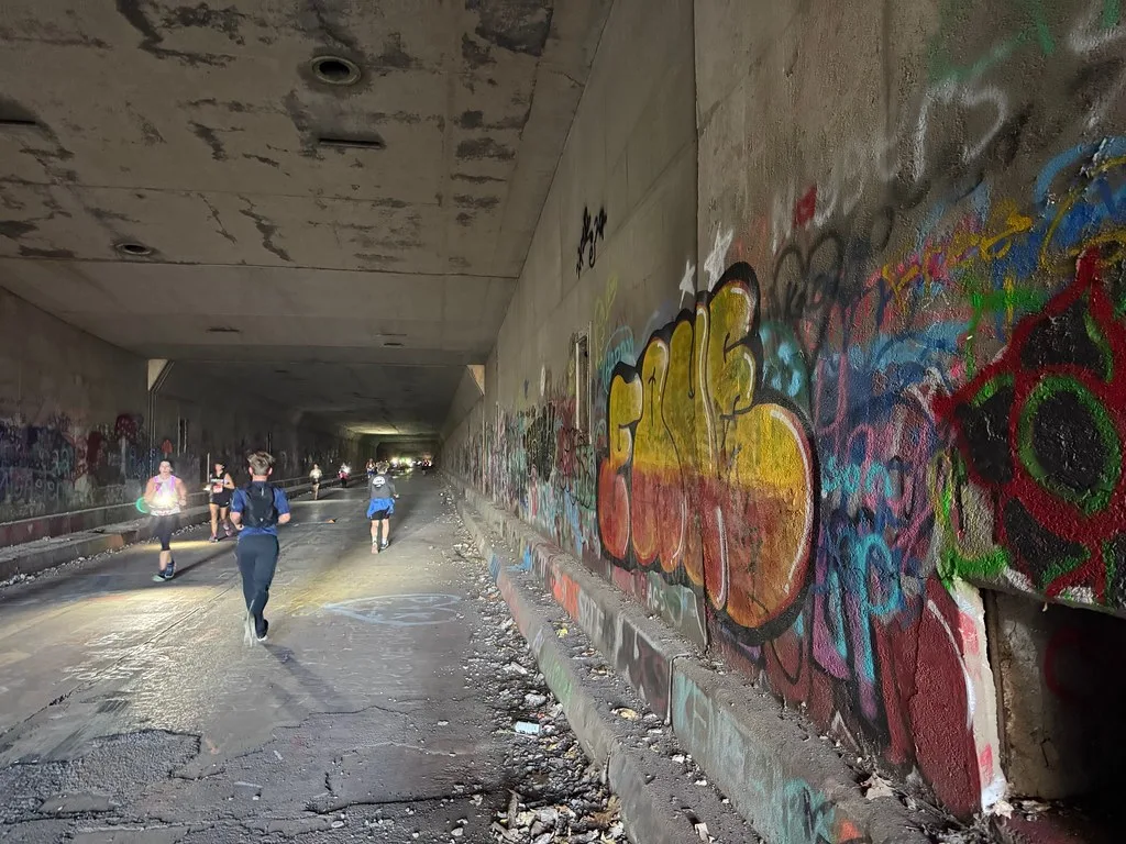 Old tunnel with graffiti-covered walls and cracked pavement, with a few passersby.
