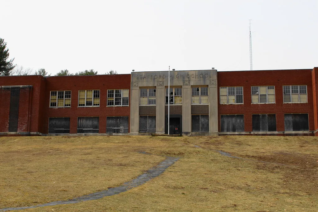 Brick facade of Stafford High School with boarded lower windows and broken upper panes.