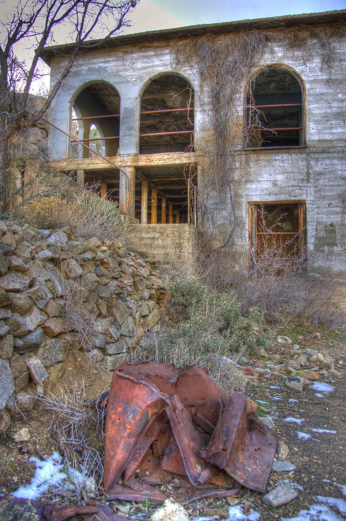 Old building with large empty arched openings behind rubble and vegetation.