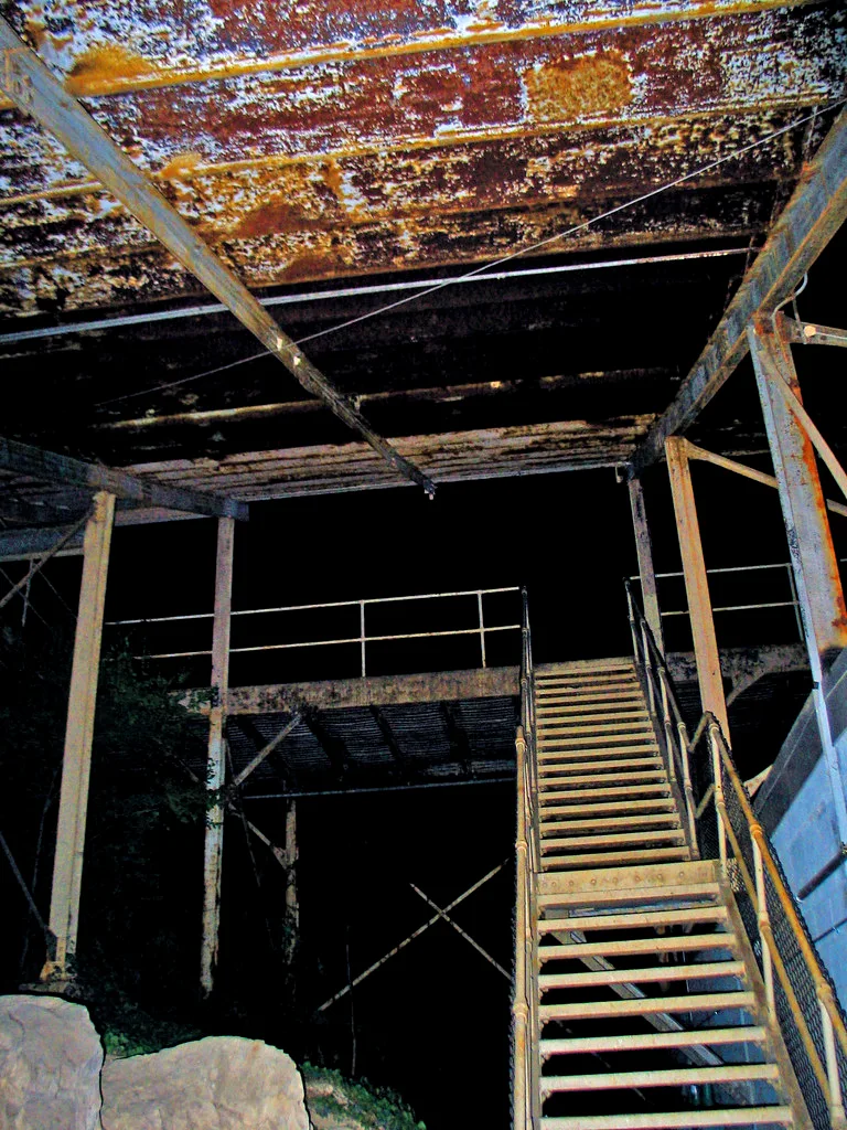 Rusty metal staircase beneath a corroded industrial ceiling in a deserted building.