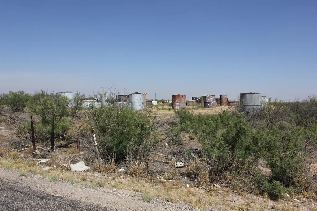 Disused former storage site with rusty cylindrical tanks among dry shrubs.