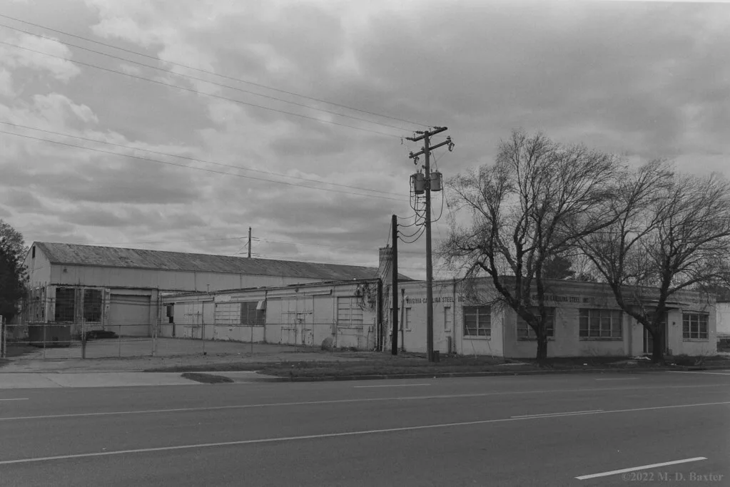 Fenced old low factory with deteriorated facades, in black and white.