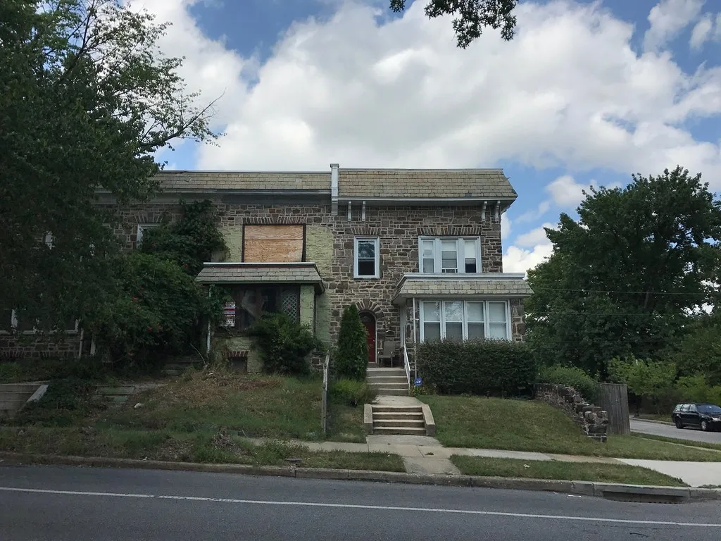 Stone row house with its left-hand section boarded up and overgrown.