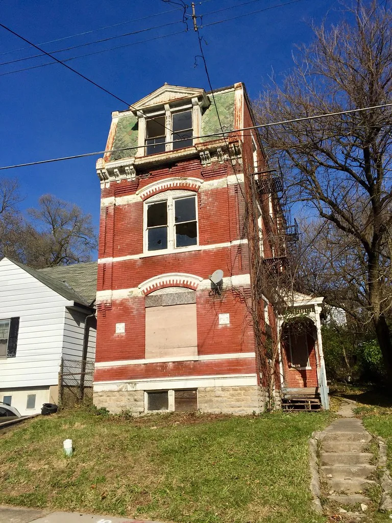 Neglected red building with broken windows and a boarded entrance.