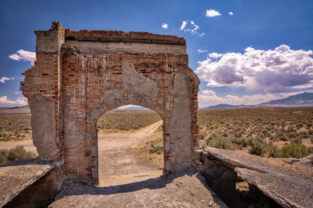 Arche de briques en ruine dans un paysage désertique.