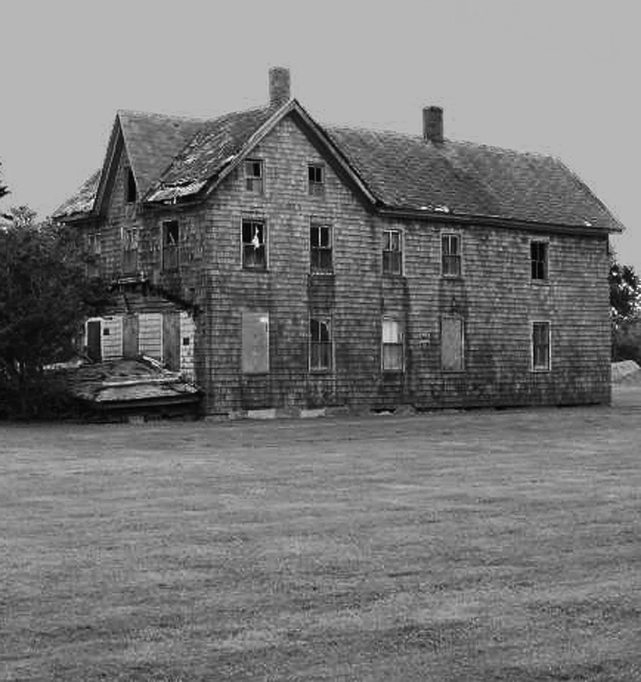Large abandoned wooden house with broken windows, in black and white.