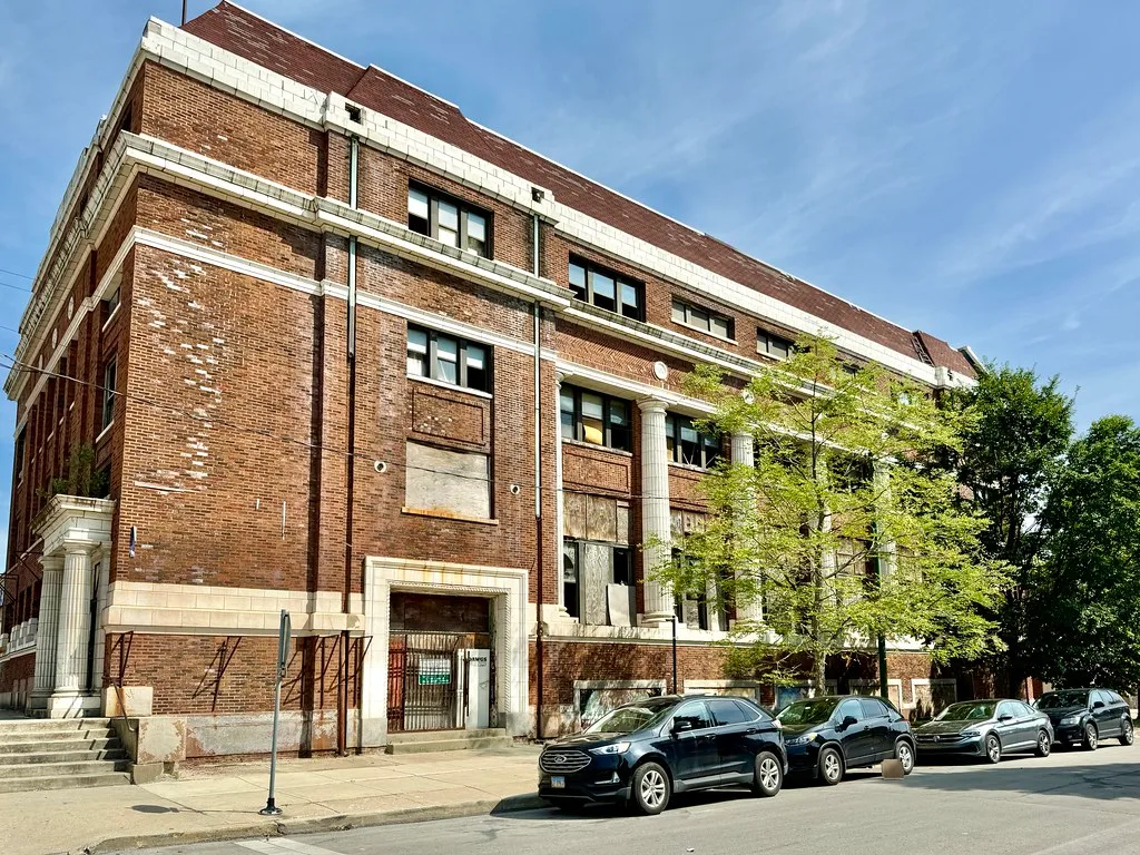 Large brick building with white columns and broken or boarded windows.