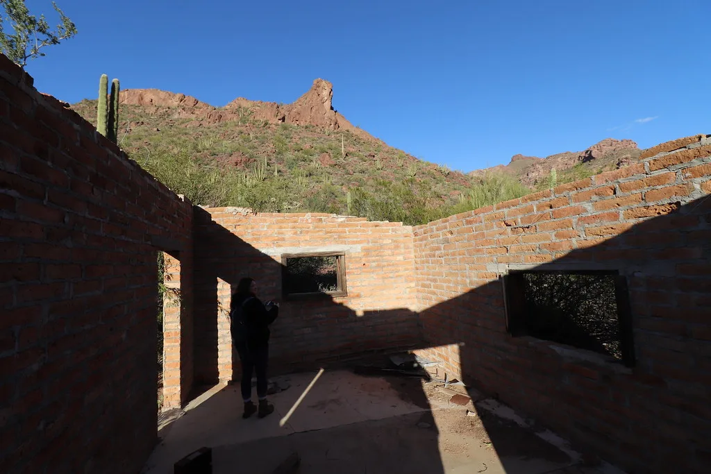Roofless interior of a brick house in a desert landscape.