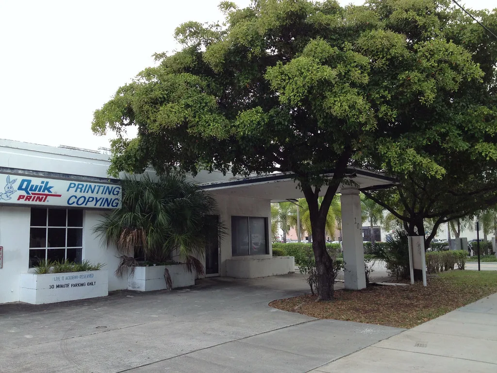 Former gas station in West Palm Beach with a canopy partly hidden by trees.