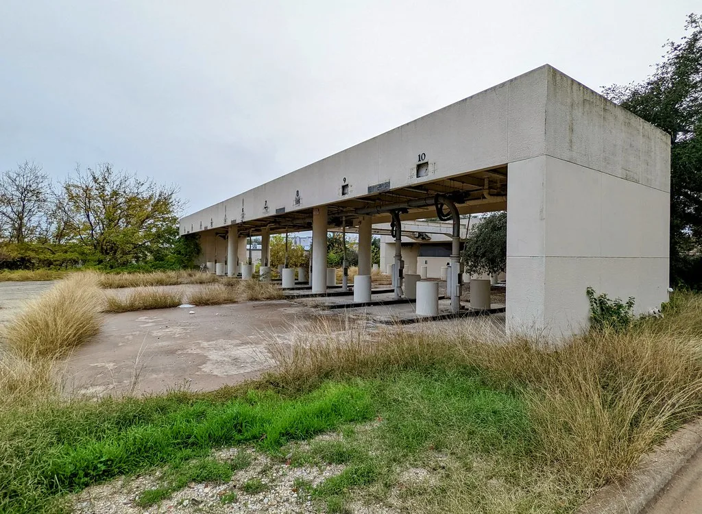 Old service canopy with several lanes overgrown with grass.