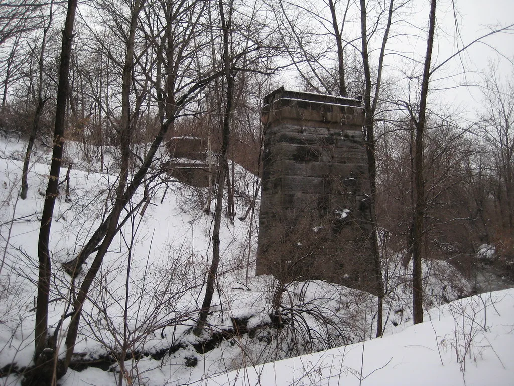 Anciennes piles de pont abandonnées en pierre sans tablier dans un ravin boisé enneigé.