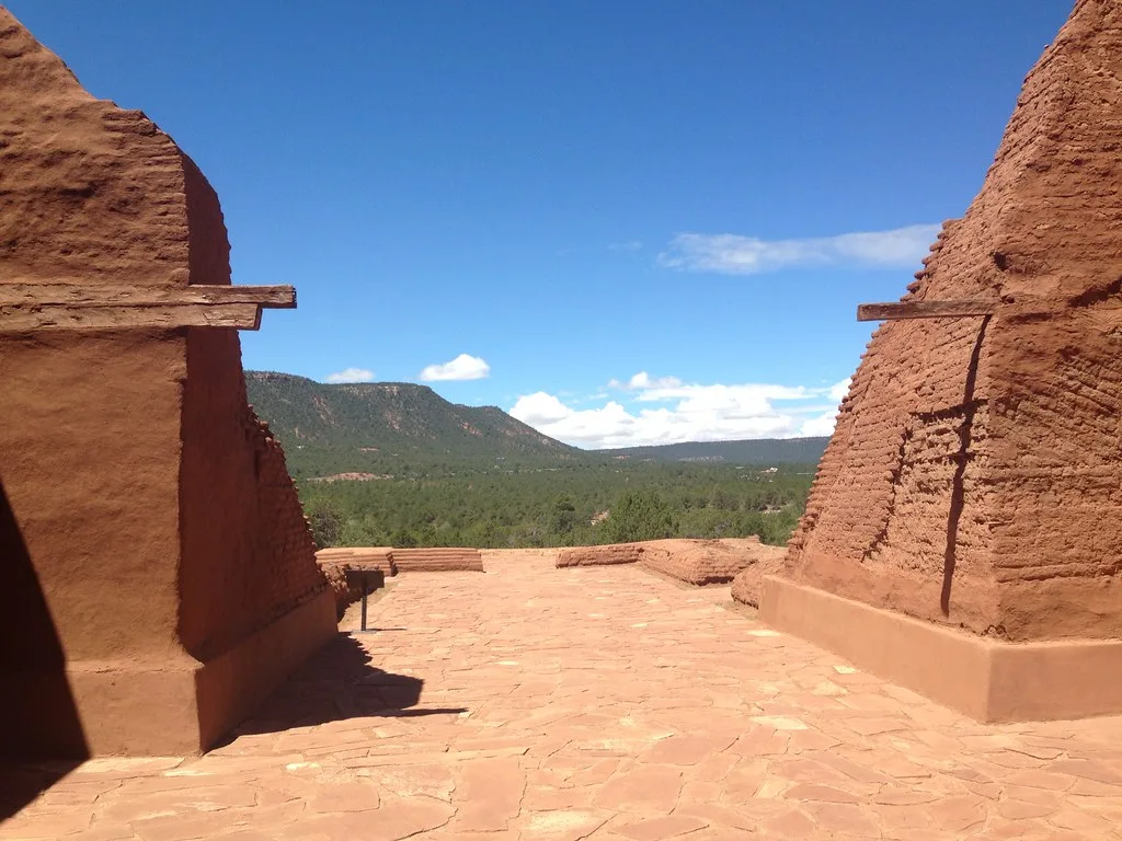 Remains of red earthen walls opening onto a wooded landscape.