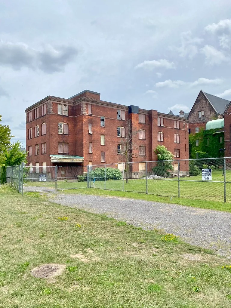Bâtiment de brique désaffecté aux fenêtres condamnées derrière une clôture de sécurité.