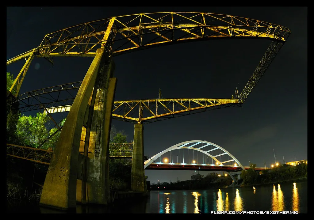 Large abandoned metal framework on pillars by the water, photographed at night.