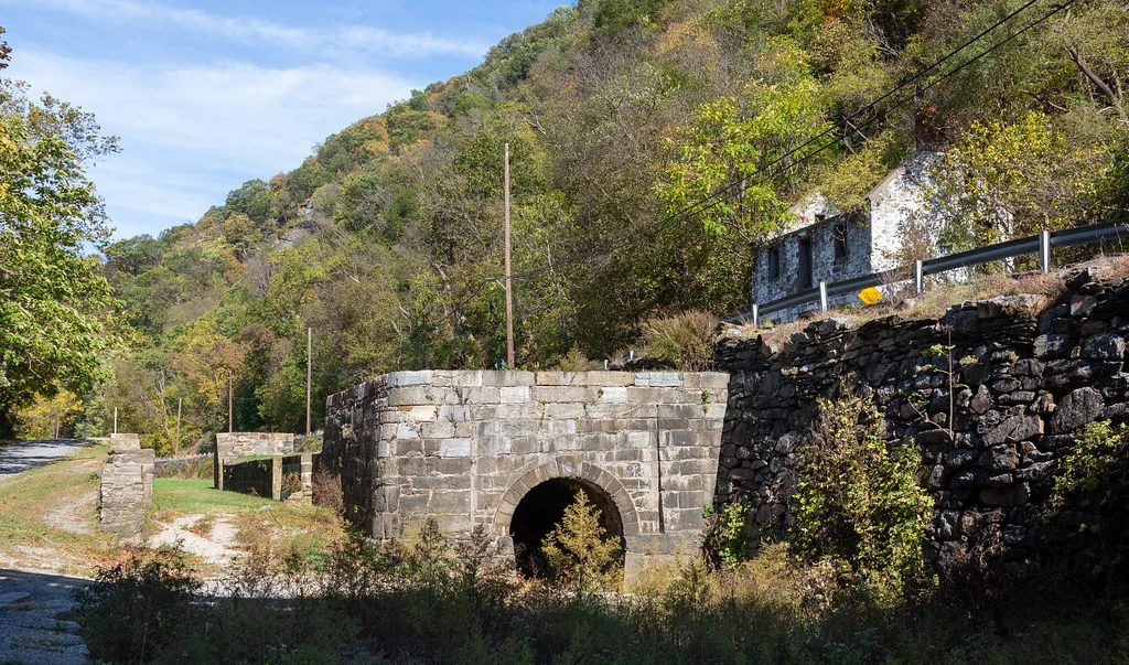 Old arched stone structure with remaining walls and a roofless ruin on the hillside.