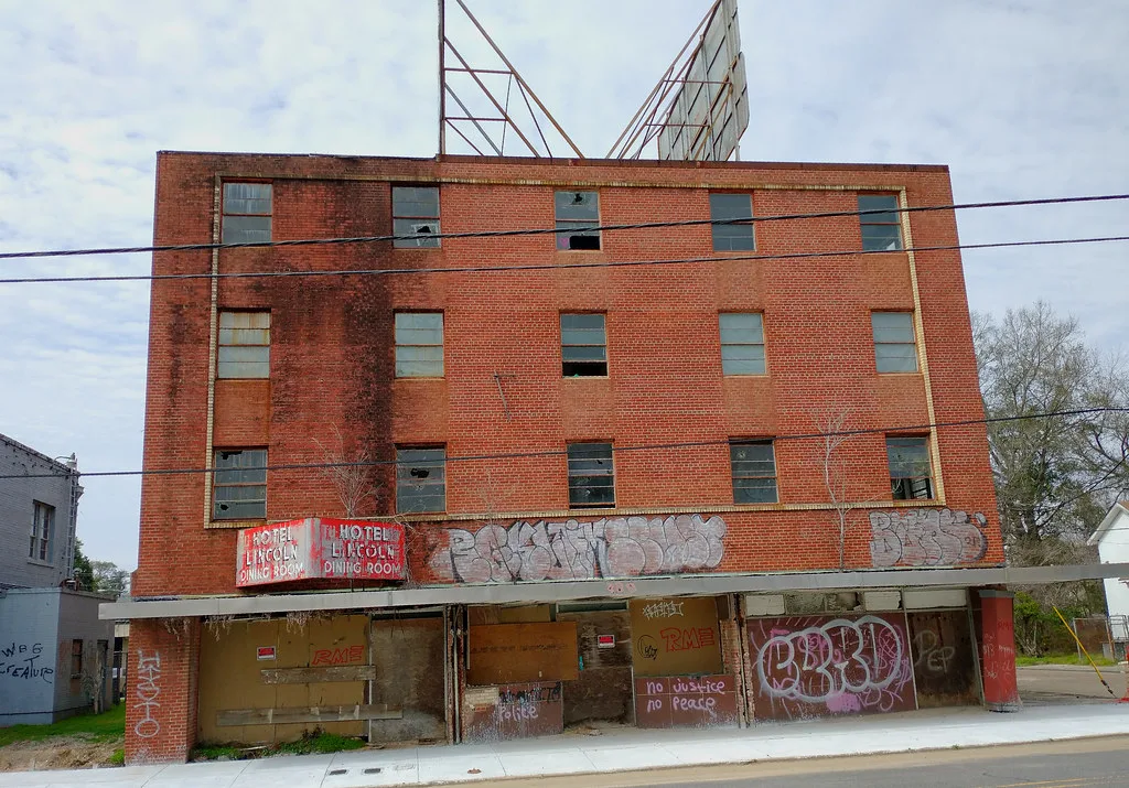 Brick facade of the Lincoln Hotel with broken windows and graffiti-covered boarded storefronts.