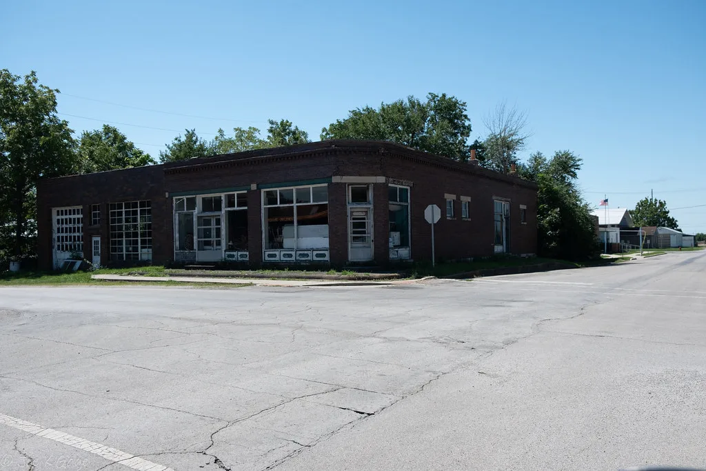 Disused old brick garage with large partly broken windows at a street corner.