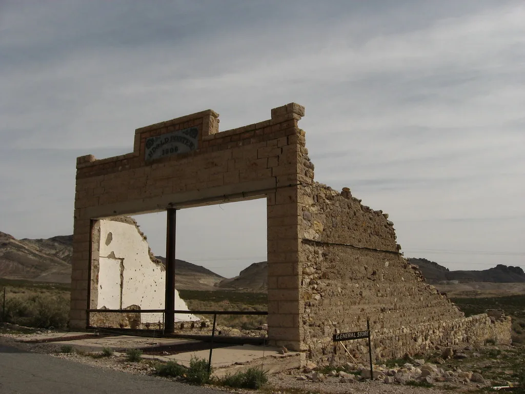 Ruine d’une ancienne boutique avec grande baie vide et mur latéral effondré dans un paysage aride.