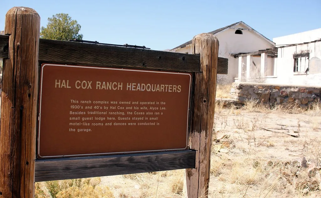 Hal Cox Ranch Headquarters sign in front of the ruined white walls of an old ranch amid dry grass.