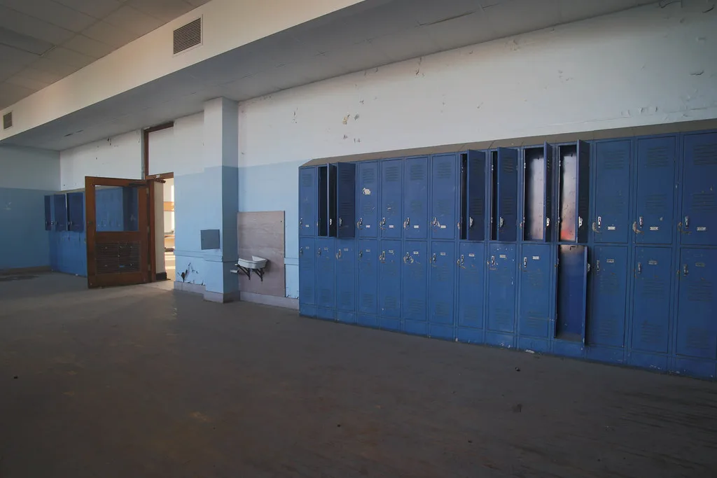 Ancien couloir scolaire avec casiers bleus abîmés et peinture écaillée.