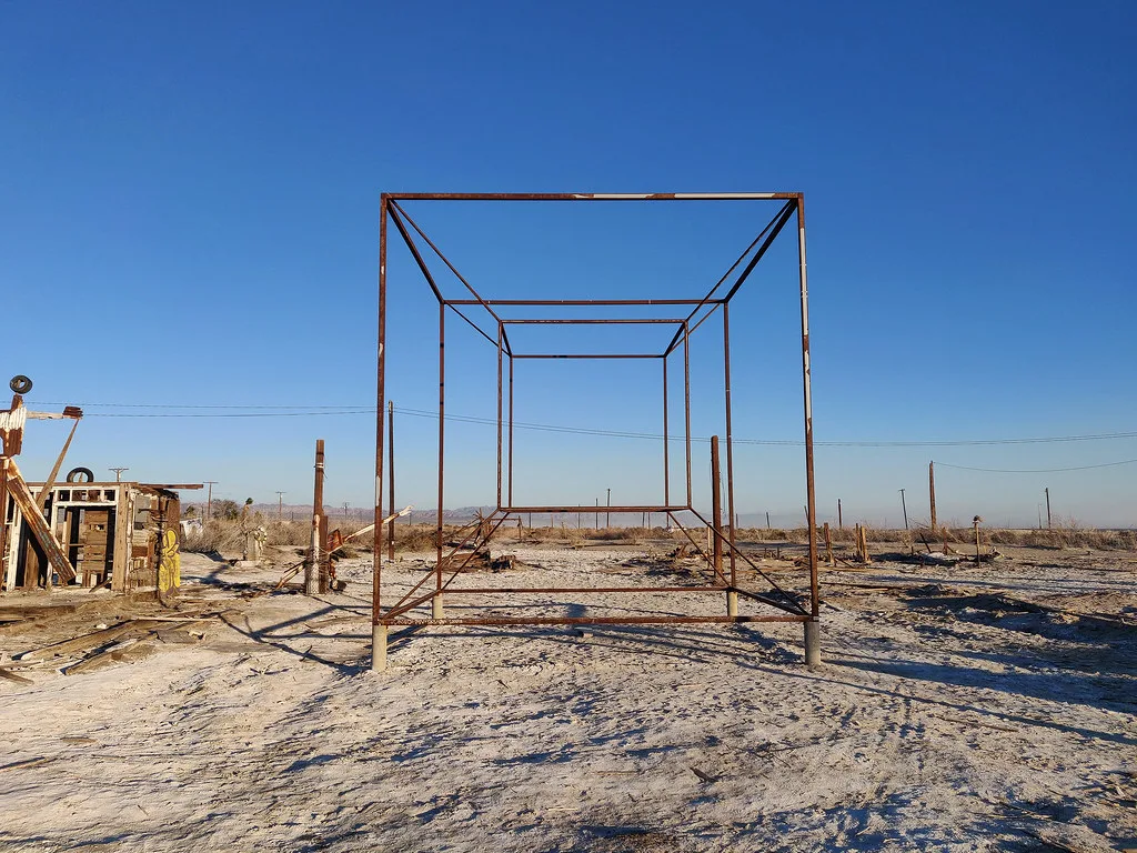 Ossature métallique rouillée d’une ancienne installation sur un terrain sableux.