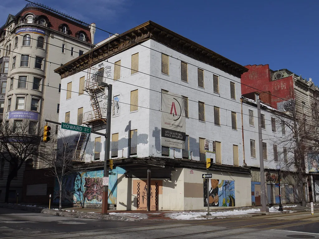 White building with boarded windows and storefronts at a junction.