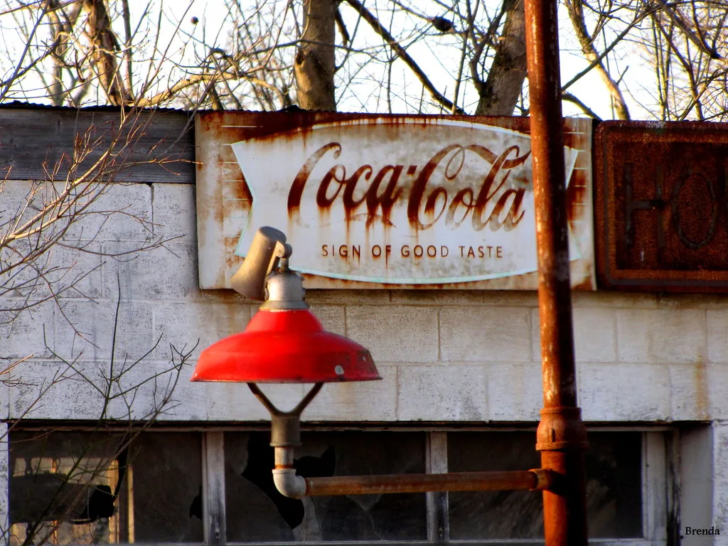 Ancienne façade aux vitres brisées avec lampe rouge et enseigne Coca-Cola usée.