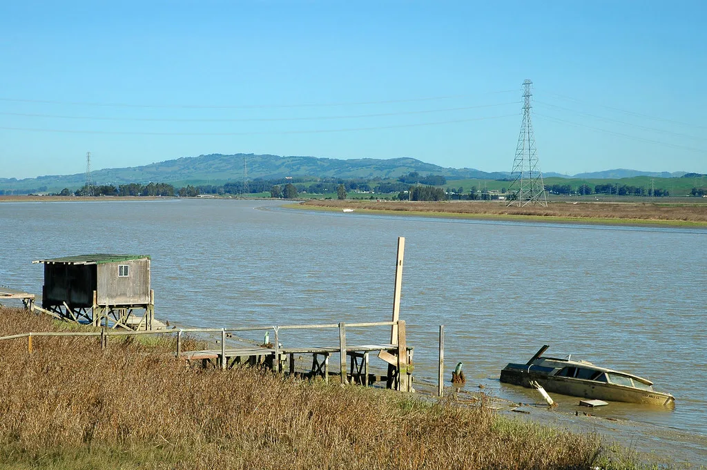 Ancien ponton et cabane en bois près d’une embarcation partiellement coulée.