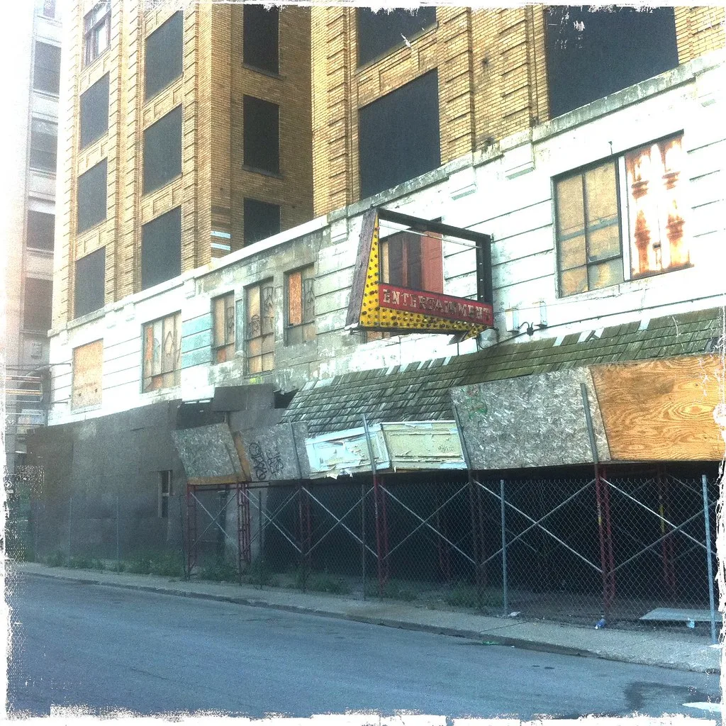 Ancienne façade condamnée avec enseigne vide derrière une clôture.