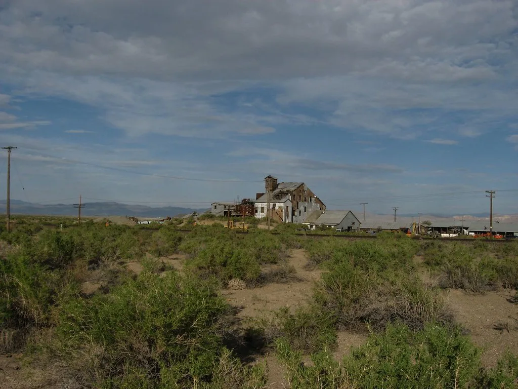 Ruined former industrial building with a collapsed roof on dry shrub-covered ground.