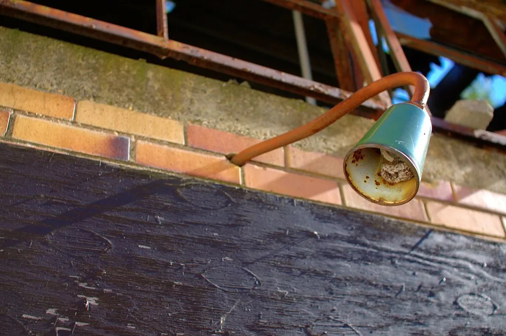 Old rusty light fixture with a nest beneath a broken window.