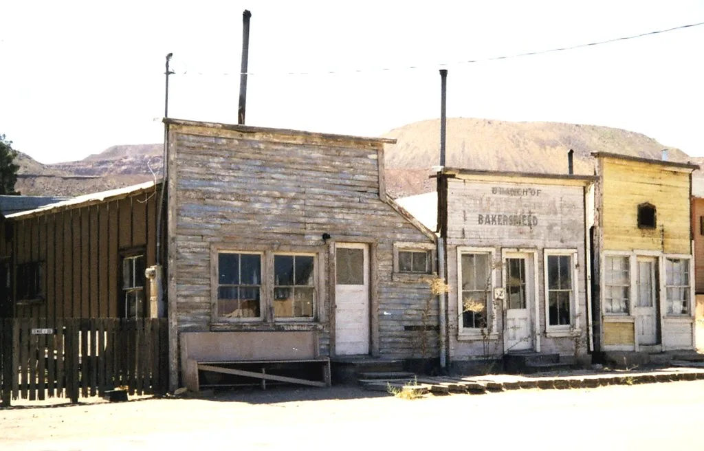 Anciens commerces de bois aux façades délavées dans un paysage sec.